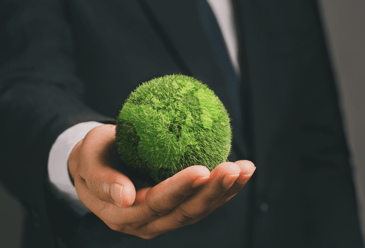 A businessman holds a green moss ball, symbolising the importance of reducing carbon emissions in precision engineering 