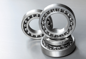 An image of two ball bearings on a stainless steel surface, used for reducing friction and supporting rotational motion. 